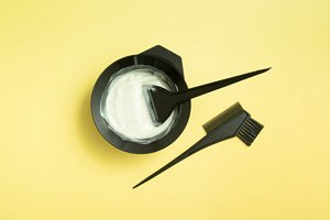 A pot of bleach with an accompanying application brush on a yellow background